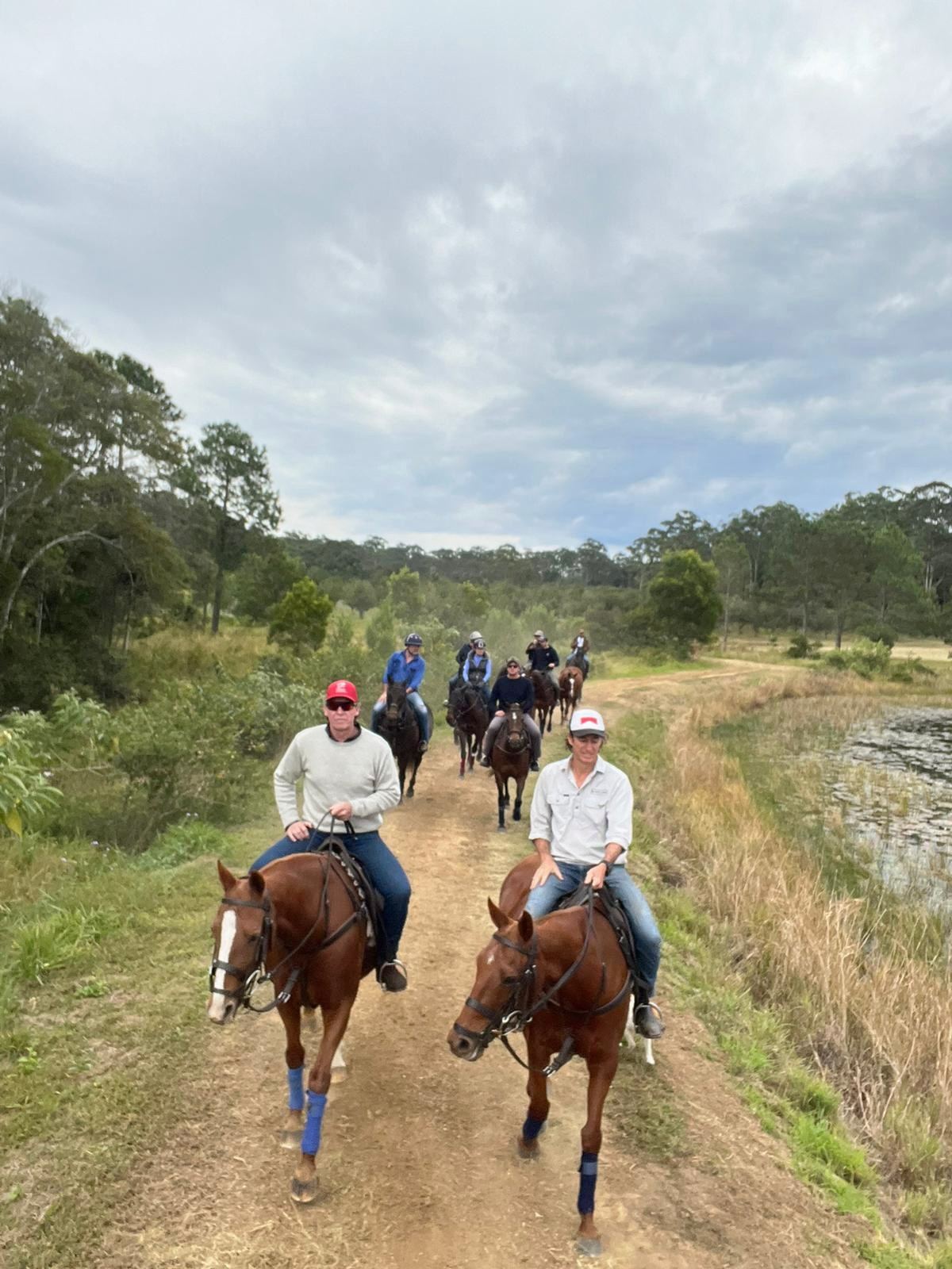 Riders on horseback along a farm track beside water